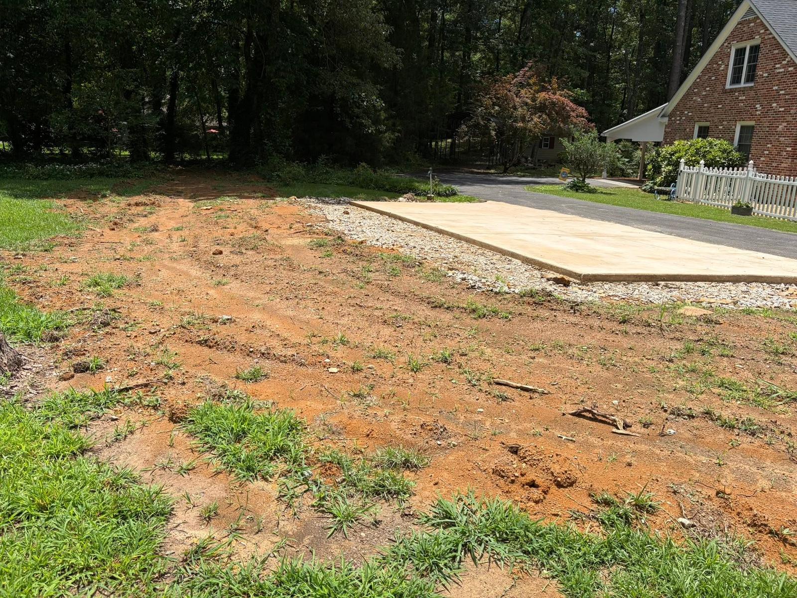 Graded red-clay pad next to a brick home