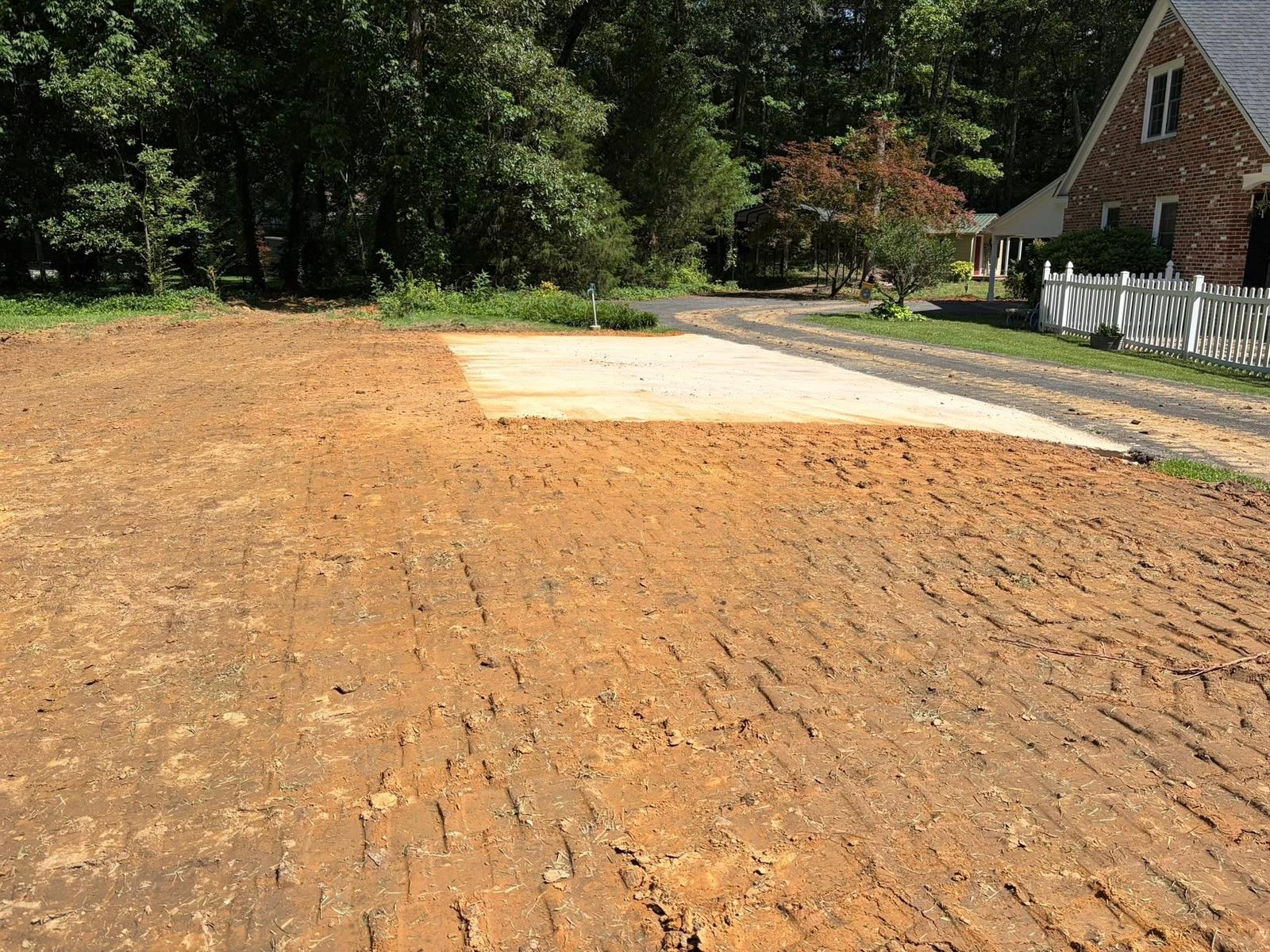 Compacted gravel driveway pad beside a white picket fence and brick home
